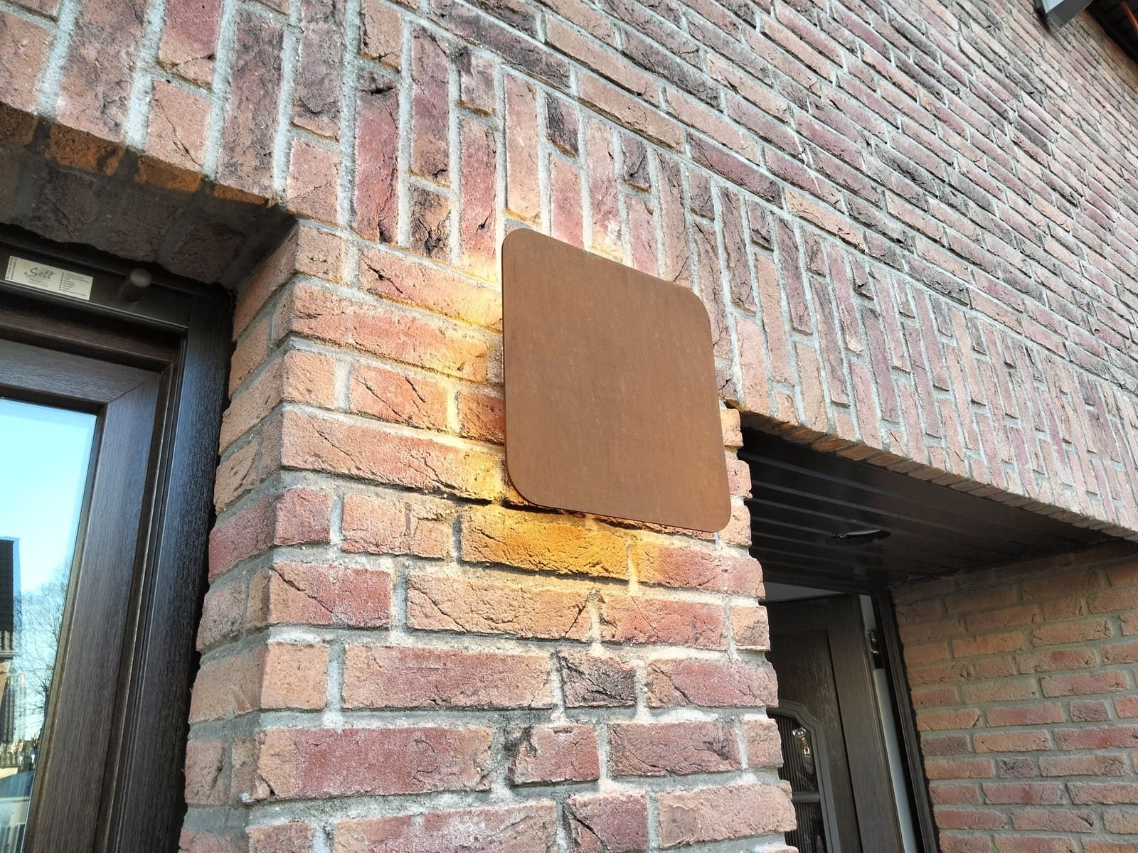 Applique extérieure carrée allumée sur un mur de briques, à côté d'une porte